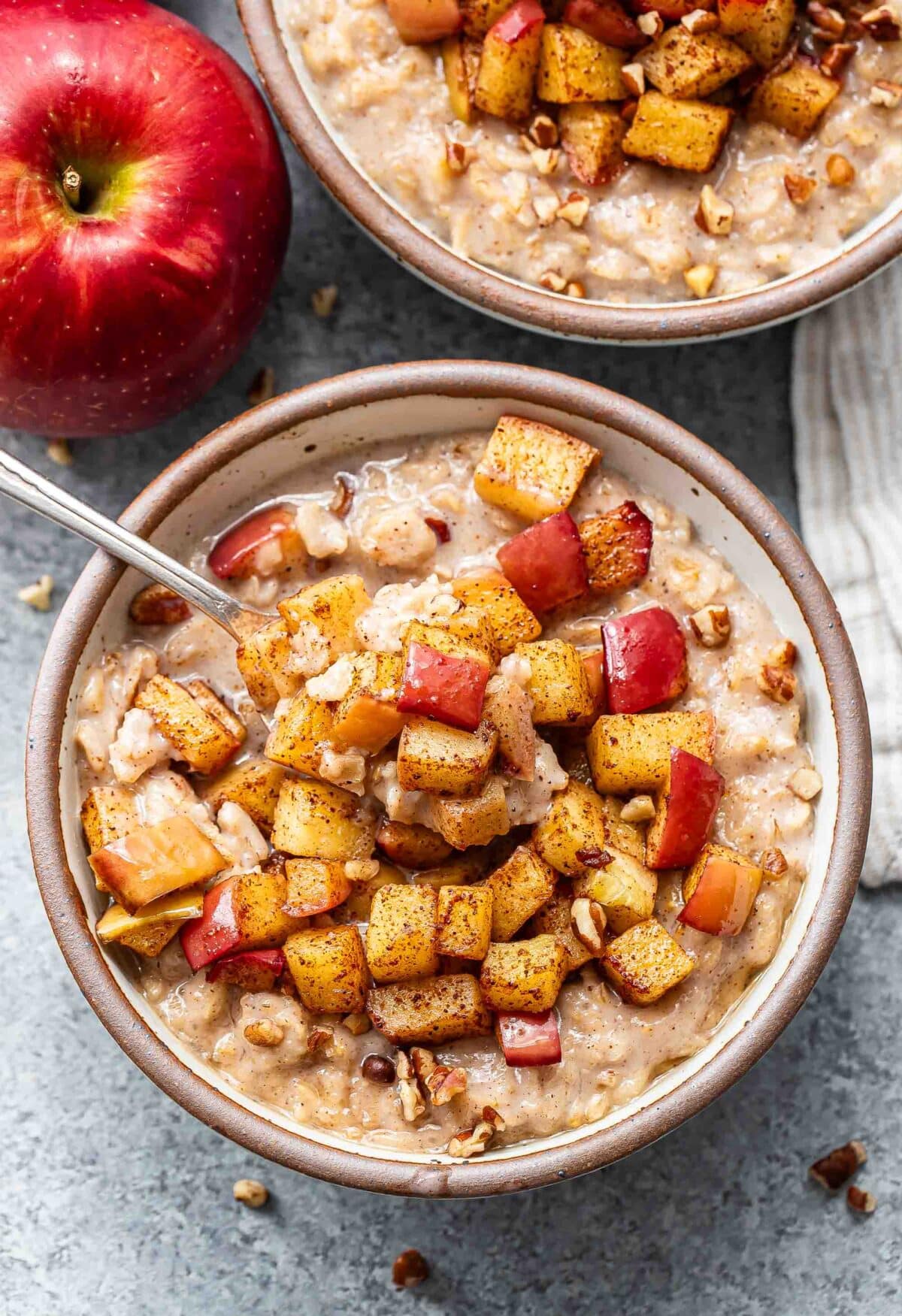 A white bowl with oatmeal topped with cinnamon apples. A spoon is in the bowl.