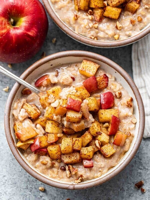 A white bowl with oatmeal topped with cinnamon apples. A spoon is in the bowl.
