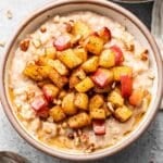 A white bowl with oatmeal topped with cinnamon apples.