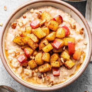 A white bowl with oatmeal topped with cinnamon apples.