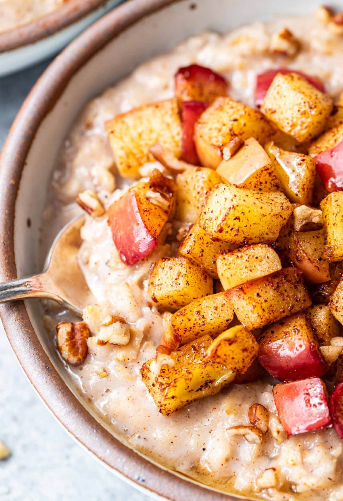 Spoon scooping up apple cinnamon oatmeal in a white bowl.