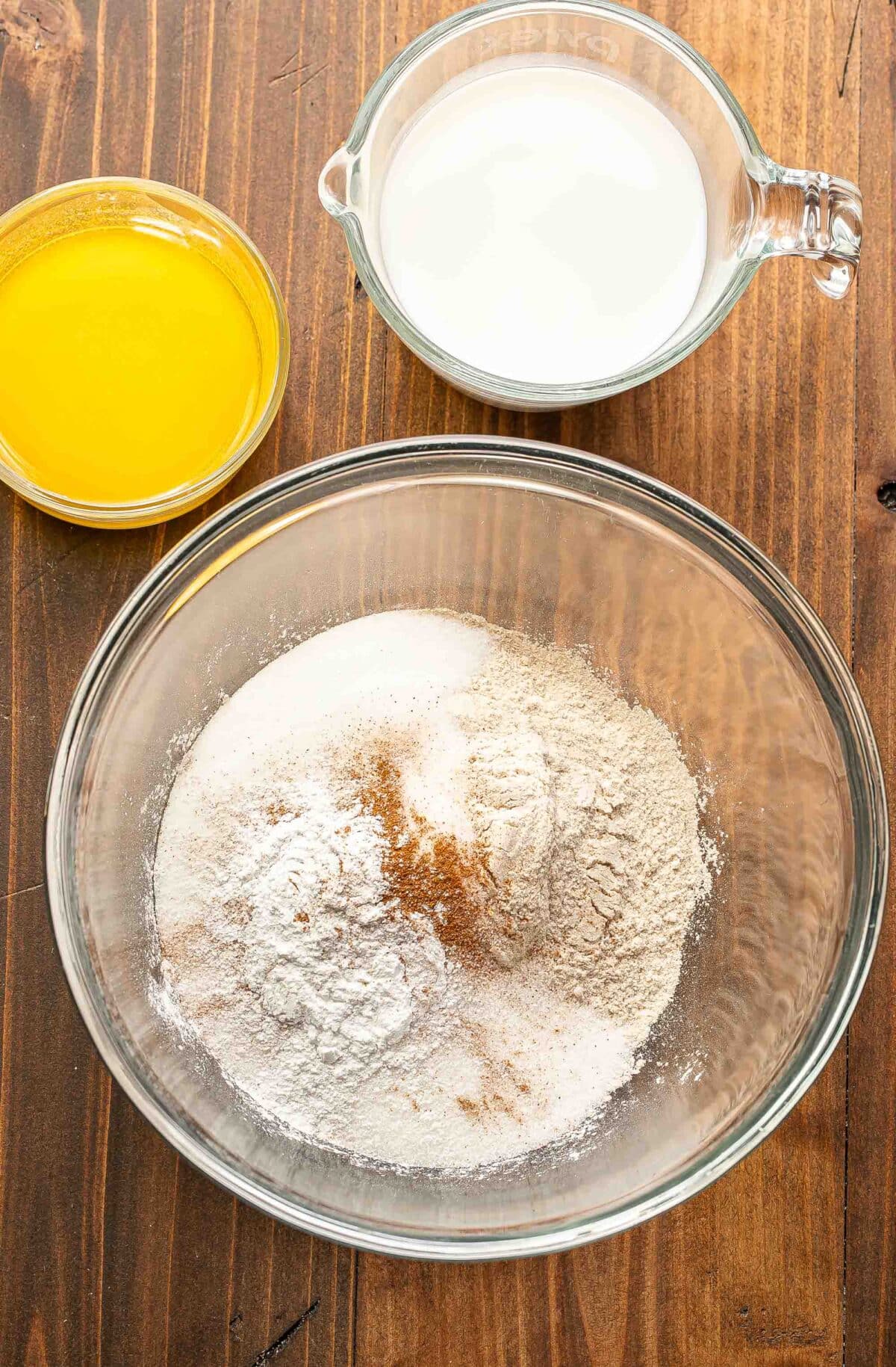 A bowl of flour, a measuring cup with milk, and a bowl of melted butter.