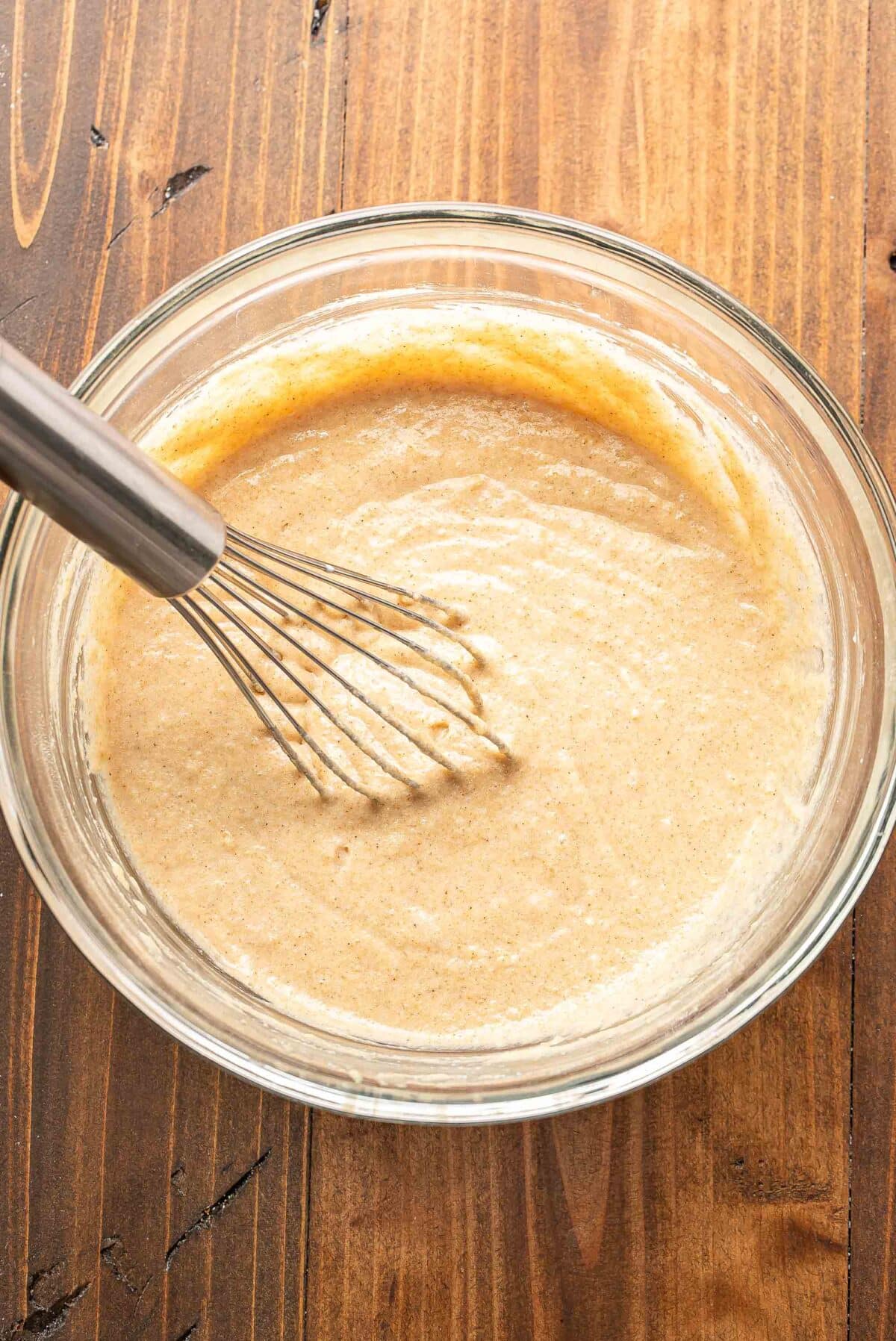 The batter for the apple cobbler in a glass bowl with a whisk.