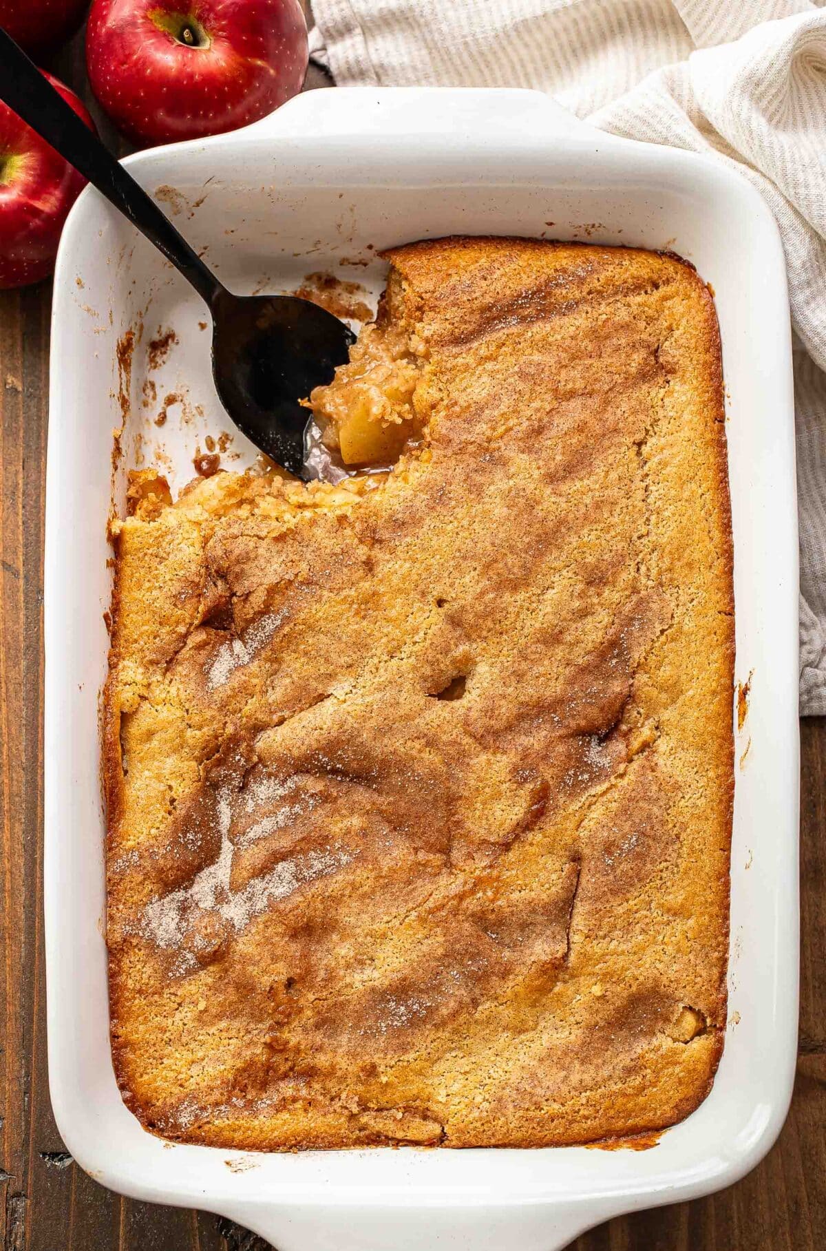 Apple cobbler in a white baking dish with a scoop cut out and a black serving spoon in it's place.