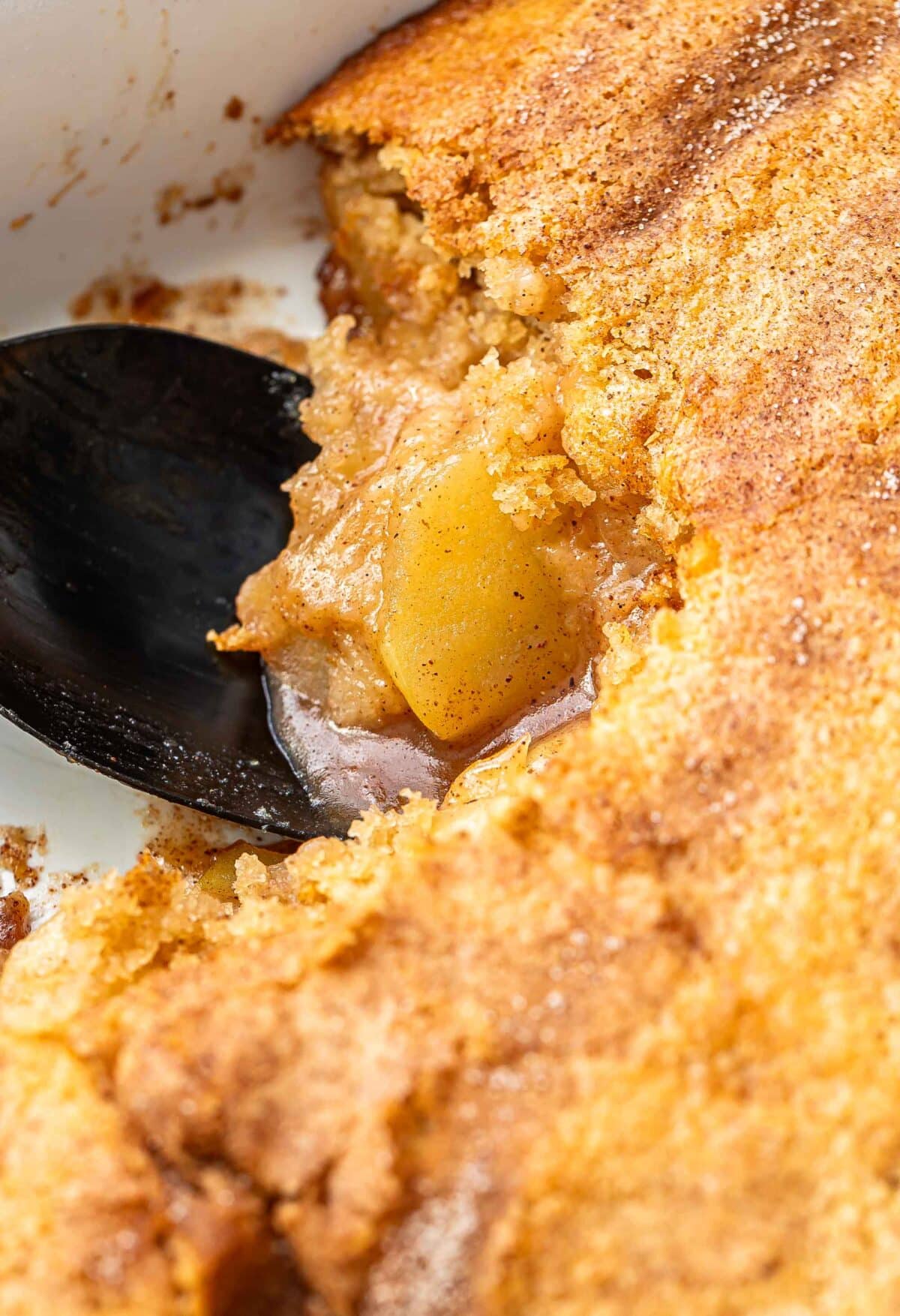 Apple cobbler in a white baking dish with a black serving spoon.