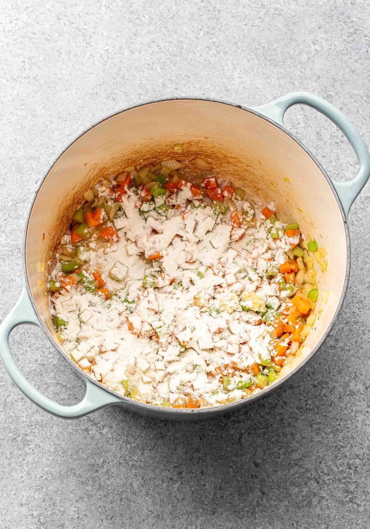 carrots, celery, and onion in a pot with flour sprinkled on top of them.