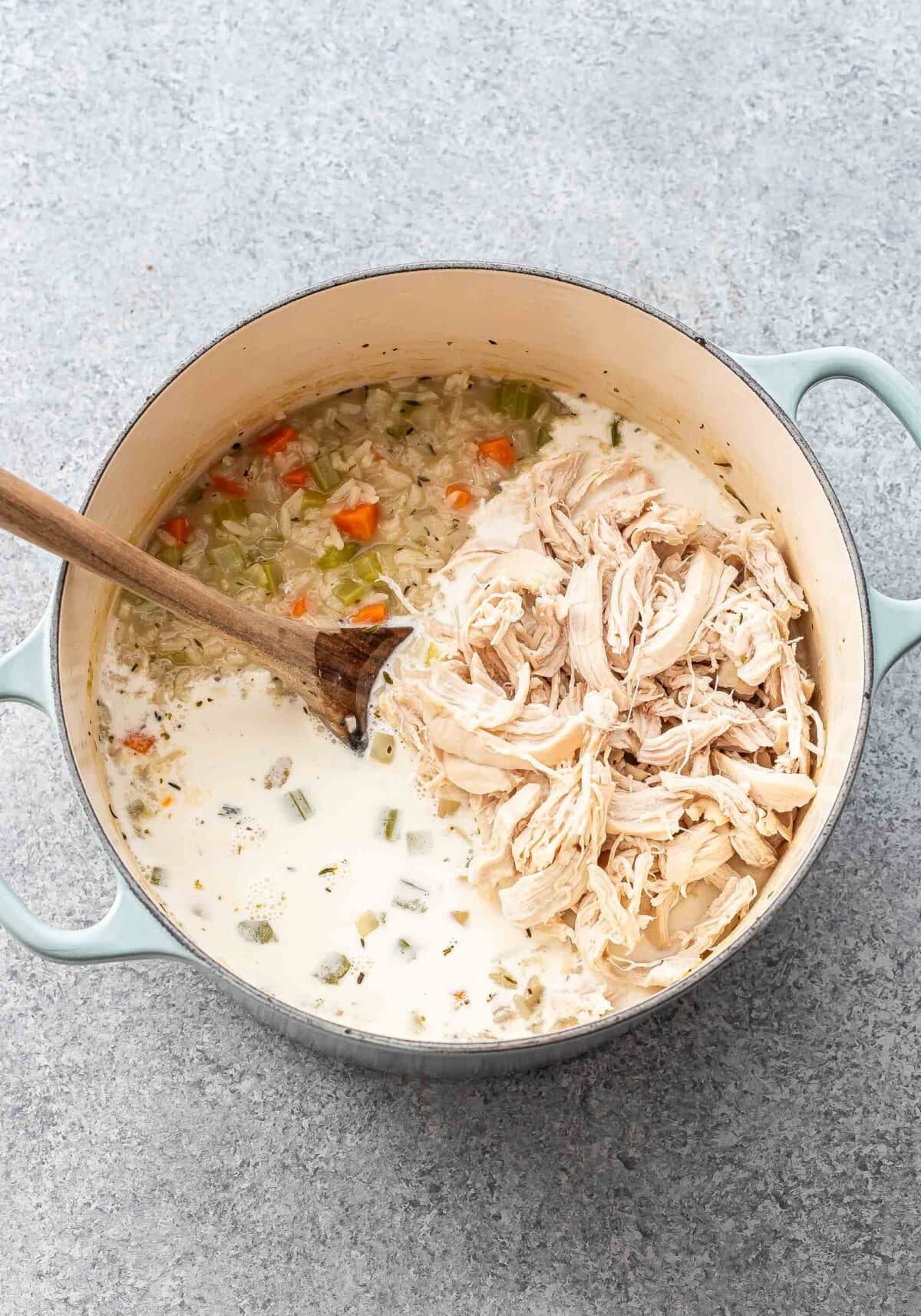 Chicken and rice soup in a pot. The shredded chicken and half and half are on top before being stirred in.