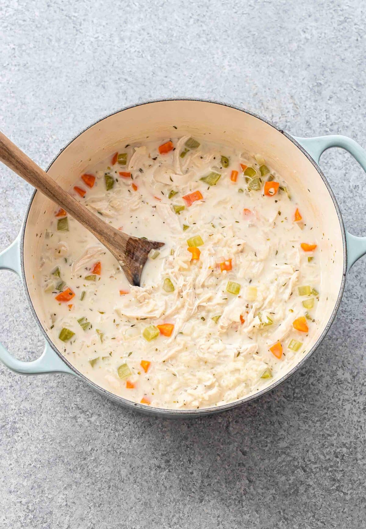 Creamy chicken and rice soup in a pot with a wooden spoon.