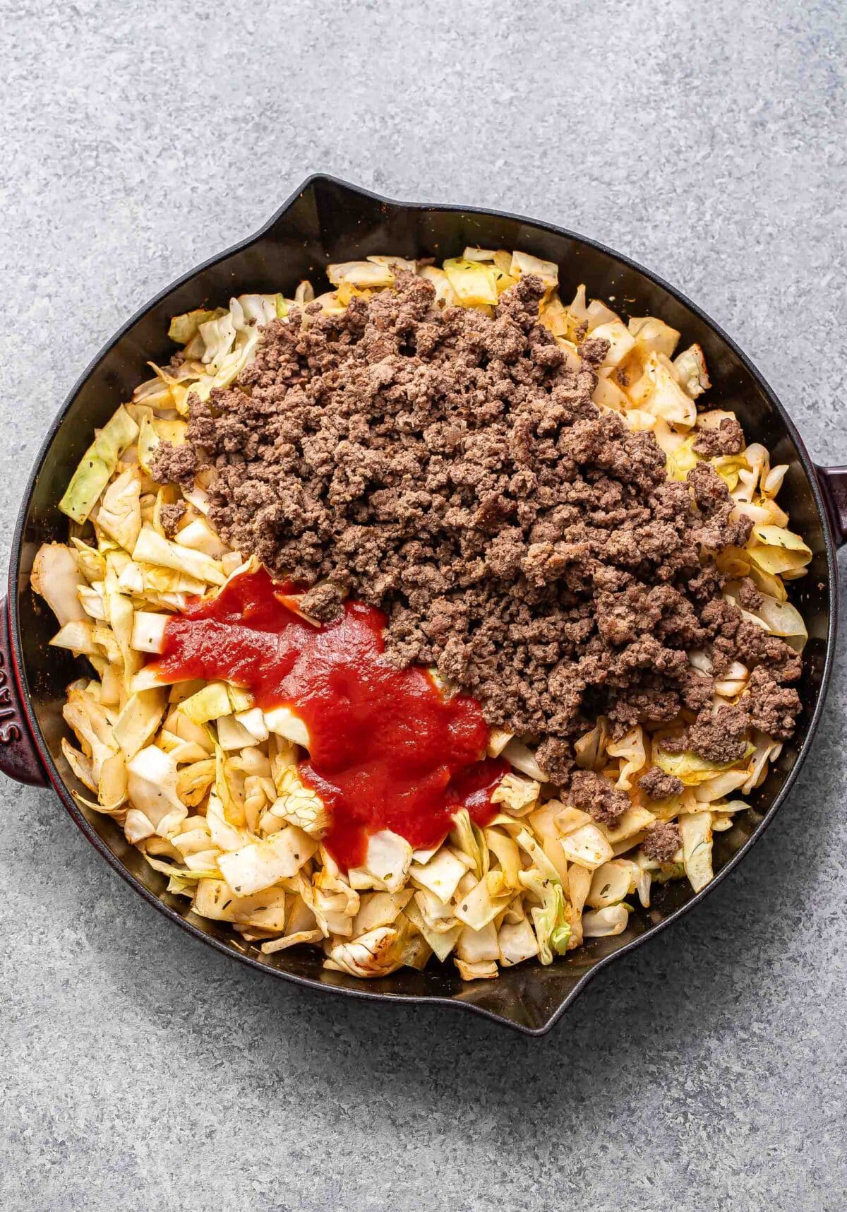 Chopped cabbage, ground beef, and tomato sauce in a skillet.