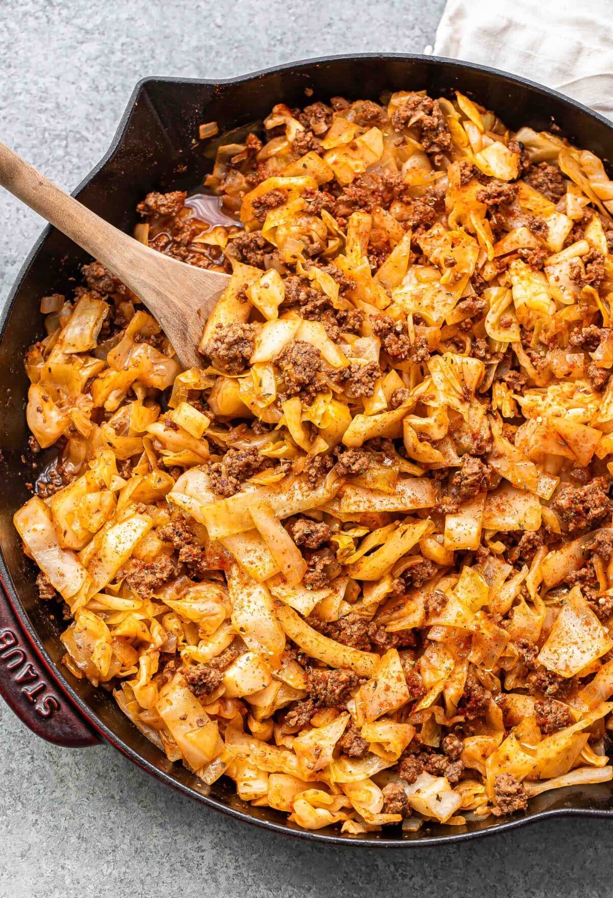 Ground beef and cabbage in a skillet with a wooden serving spoon.