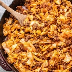 Ground beef and cabbage in a skillet with a wooden serving spoon.