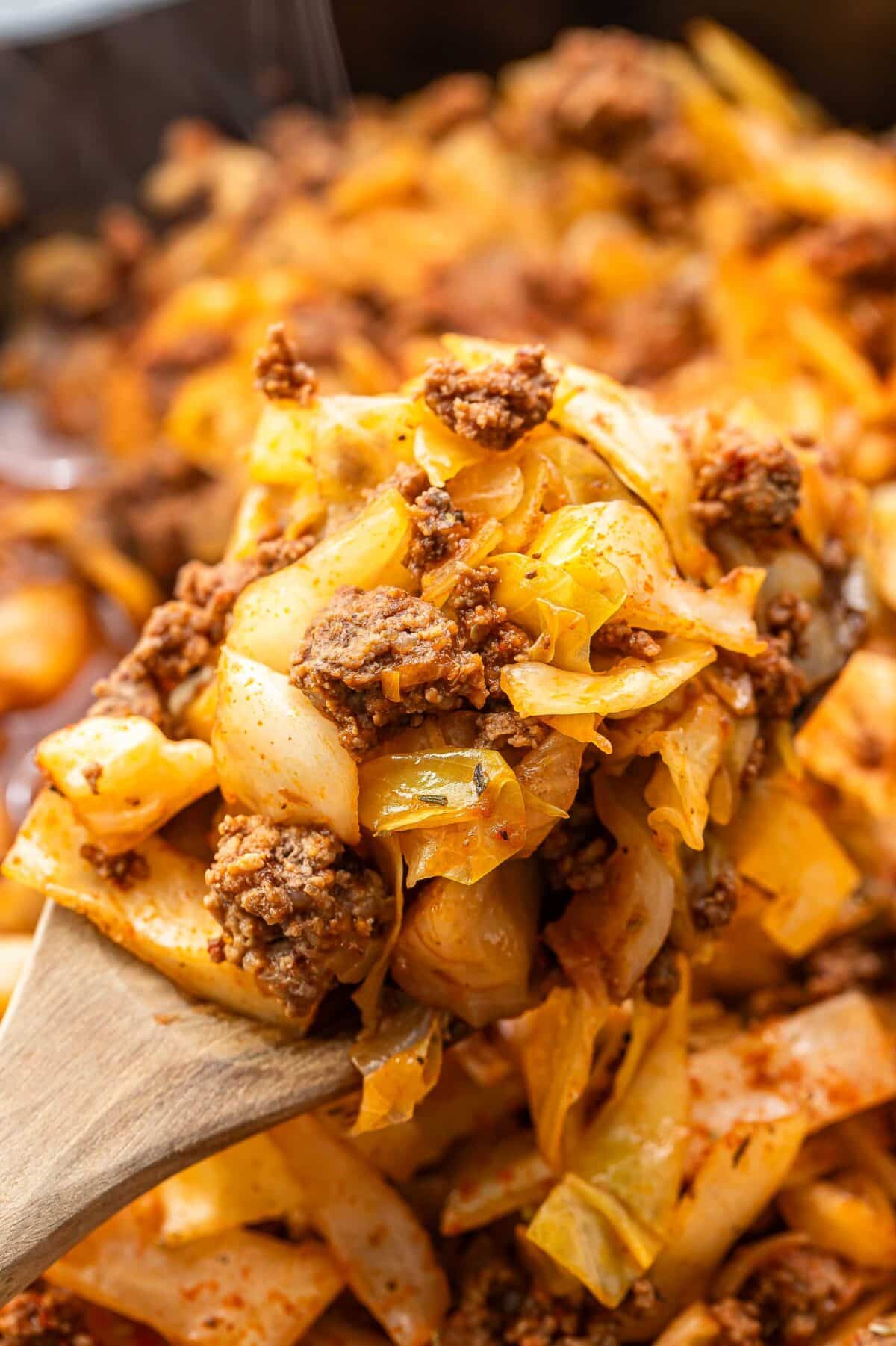 A wooden serving spoon with ground beef and cabbage on it.