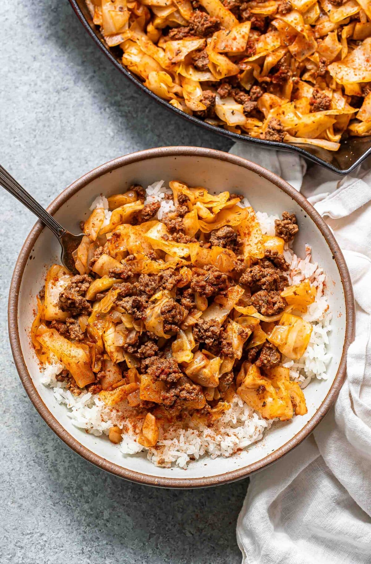 A white bowl with rice, ground beef and cabbage.