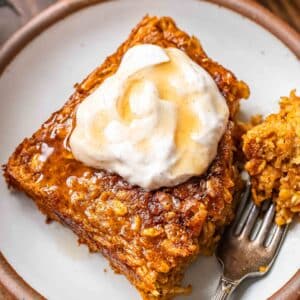 A piece of pumpkin baked oatmeal on a white plate. A corner of the oatmeal is cut off and on a fork.
