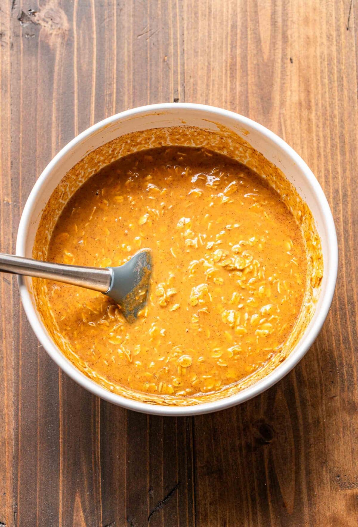 Pumpkin baked oatmeal batter in a mixing bowl with a rubber spatula.