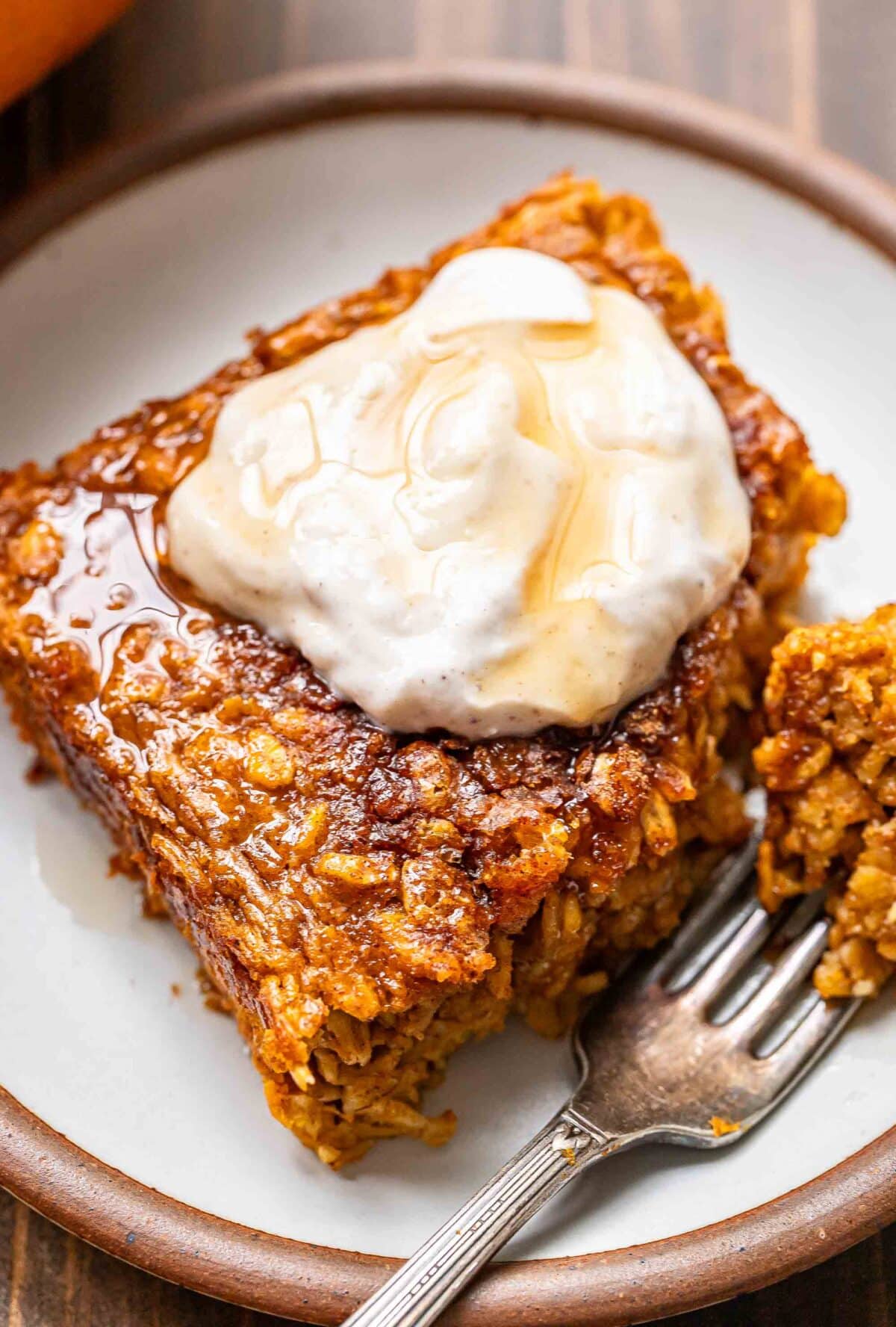A piece of pumpkin baked oatmeal topped with Greek yogurt on a white plate. A corner of the oatmeal is cut off and on a fork.