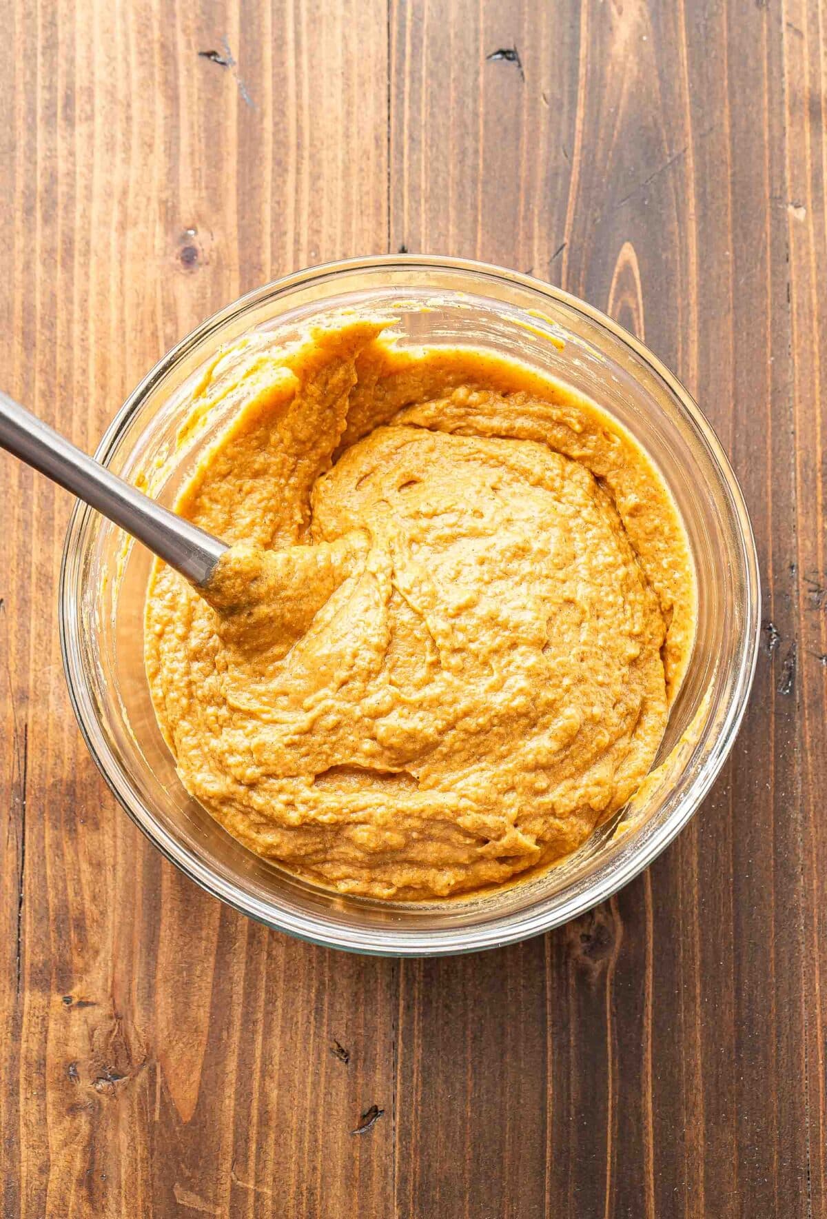 Pumpkin muffin batter in a glass mixing bowl with a spatula.