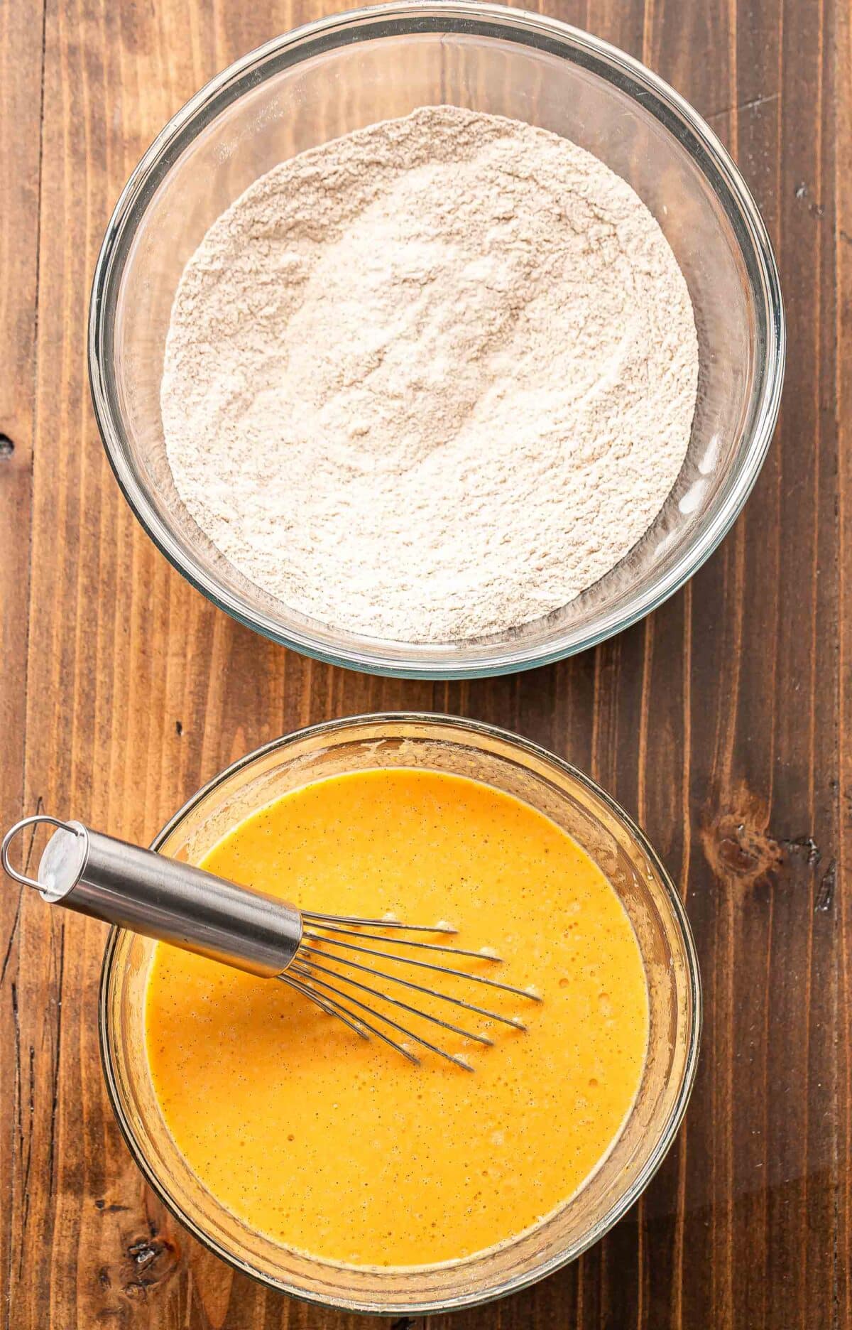 A glass bowl with flour in it and a second bowl with the wet ingredients for pumpkin pancakes in it.