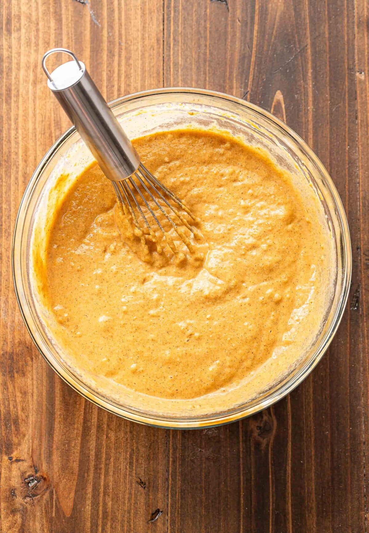 Pumpkin pancakes batter in a glass mixing bowl with a whisk.