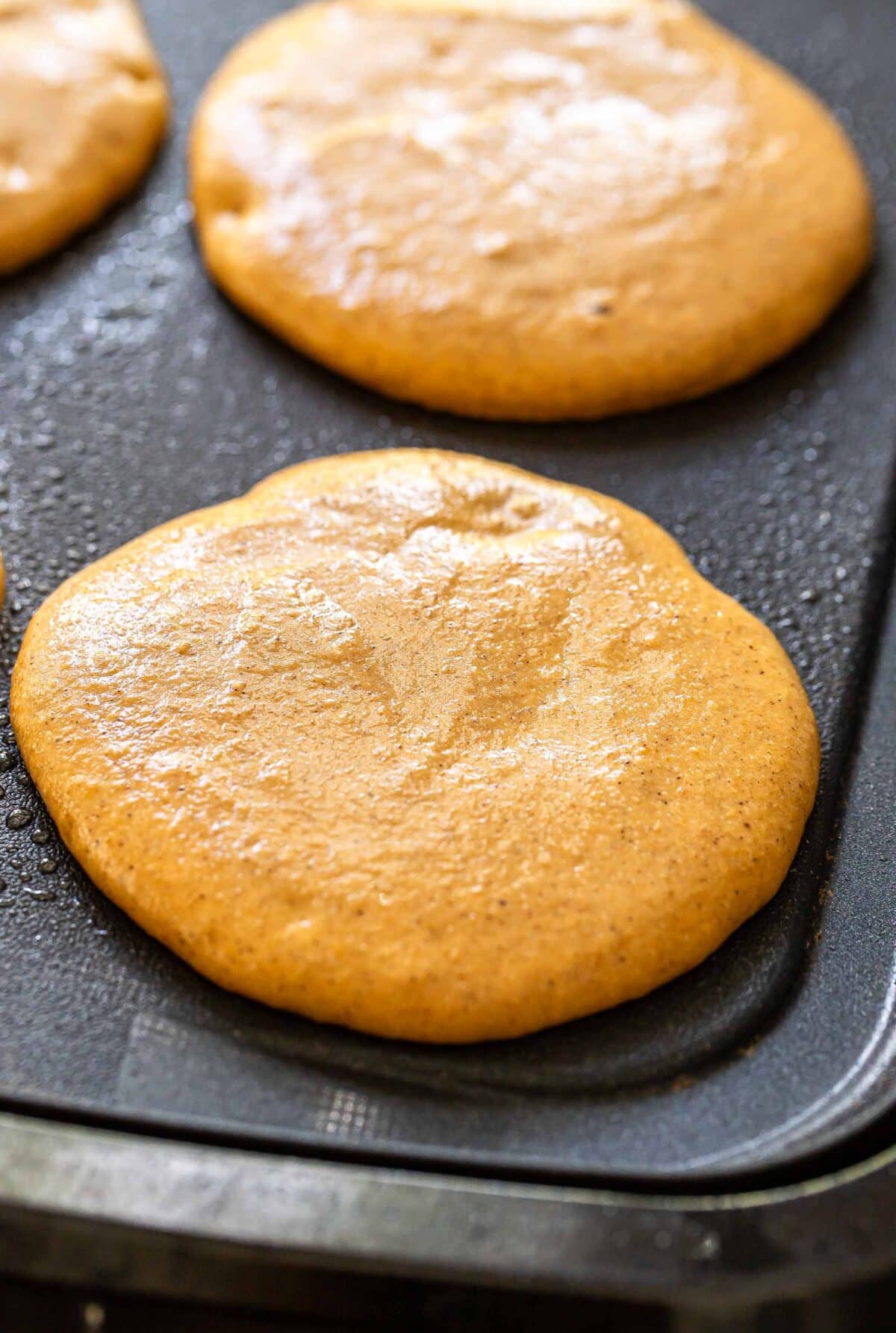 Pumpkin pancakes cooking on a griddle.