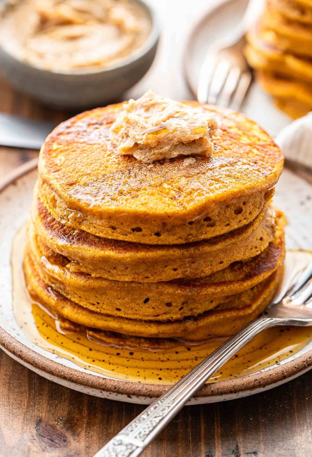 A stack of pumpkin pancakes with cinnamon sugar butter and maple syrup on top of them. 