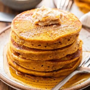 A stack of pumpkin pancakes with cinnamon sugar butter and maple syrup on top of them.