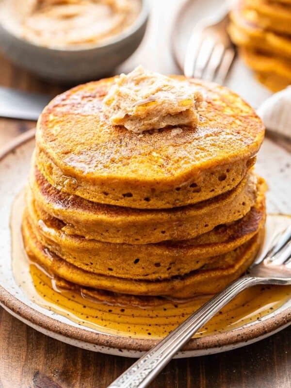A stack of pumpkin pancakes with cinnamon sugar butter and maple syrup on top of them.
