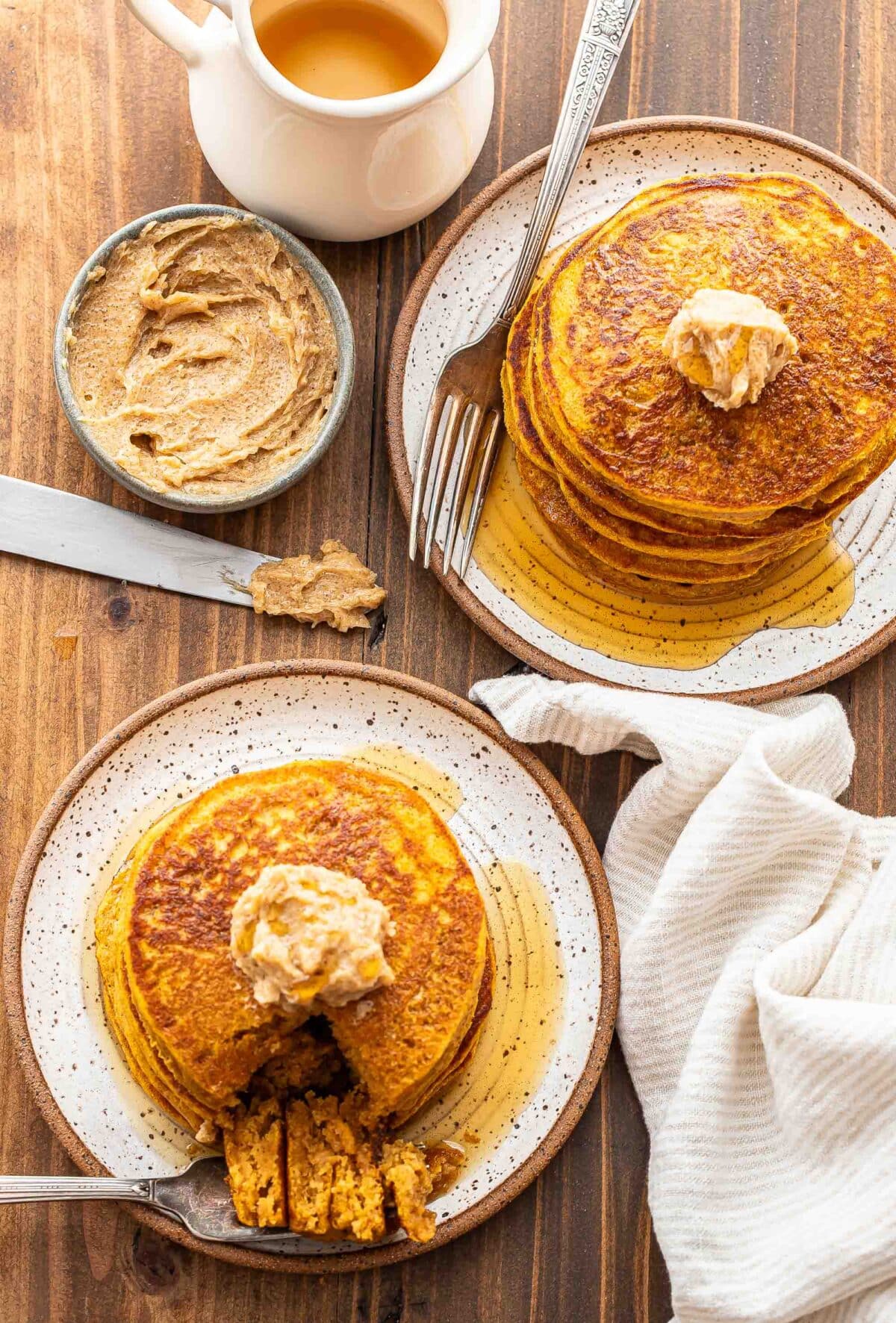 Two white plates with stacks of pumpkin pancakes on them that are topped with cinnamon sugar butter and maple syrup.