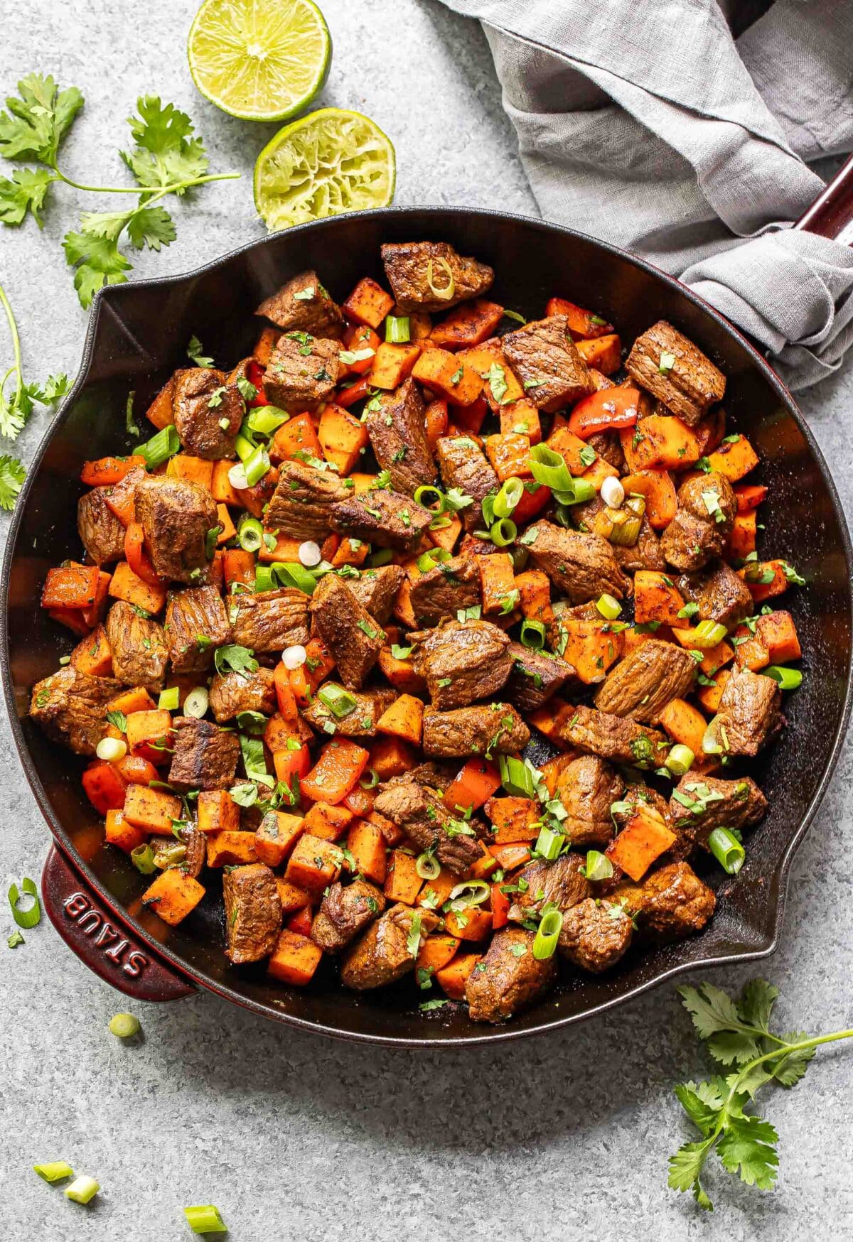 Cooked steak and sweet potatoes in a skillet with cilantro and sliced green onions on top.