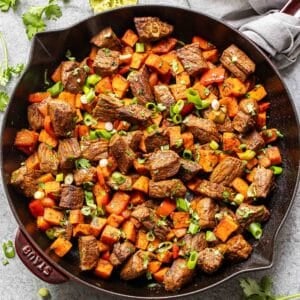 Cooked steak and sweet potatoes in a skillet with cilantro and sliced green onions on top.