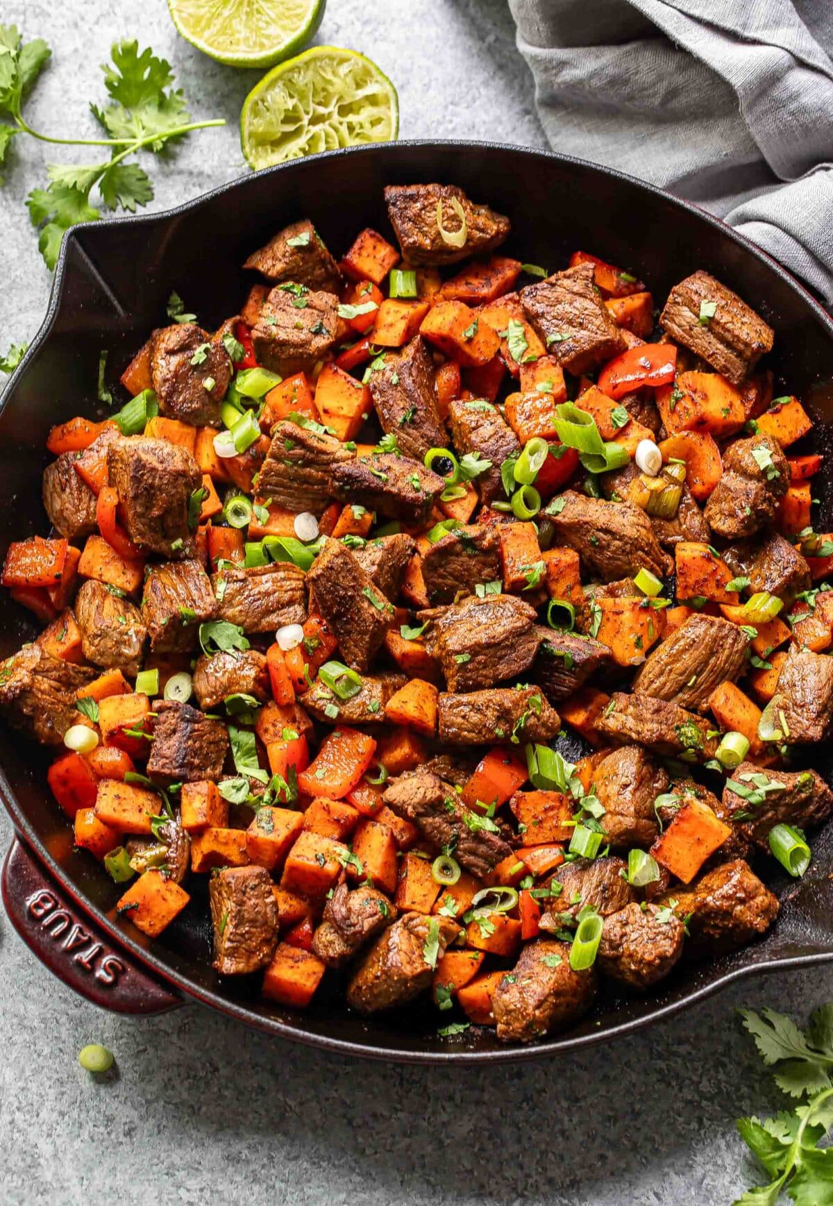 Chunks of steak, sweet potatoes, and red bell pepper in a skillet.