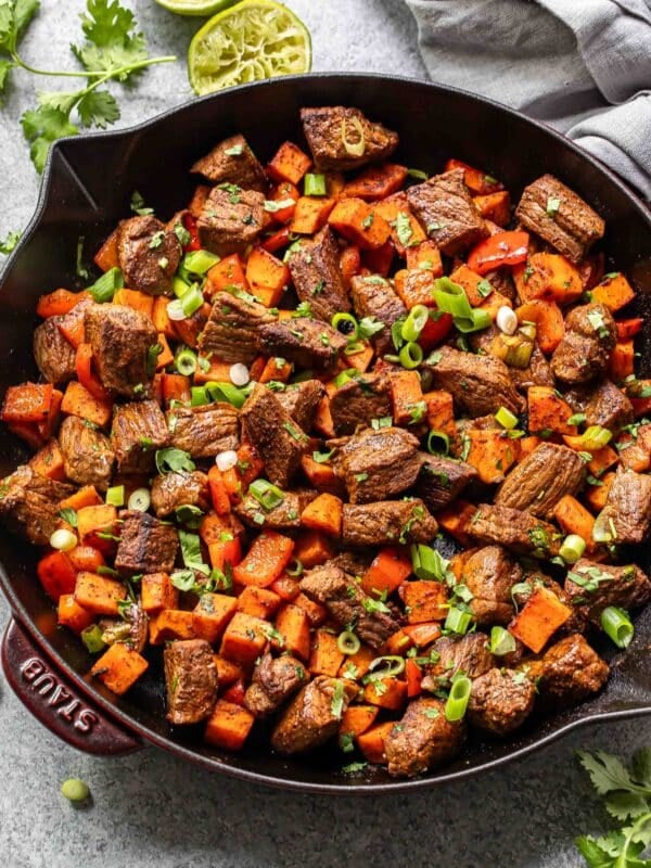 Chunks of steak, sweet potatoes, and red bell pepper in a skillet.
