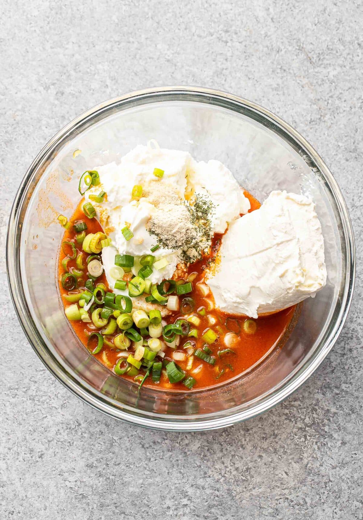 Ingredients for buffalo chicken dip in a glass mixing bowl before being whisked together.