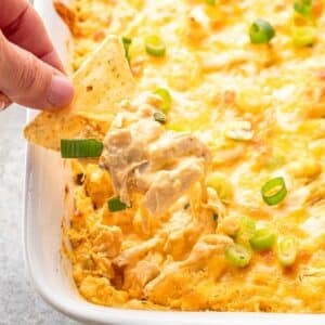 Tortilla chip scooping up buffalo chicken dip out of a casserole dish.