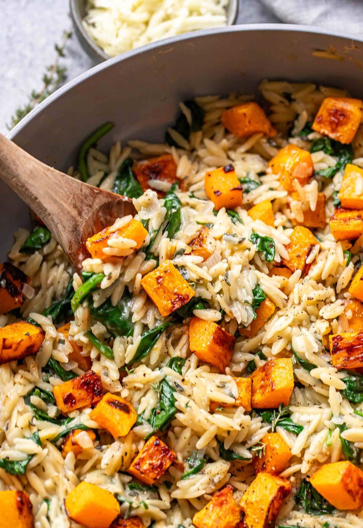 Orzo spinach and butternut squash in a pot with a wooden spoon.