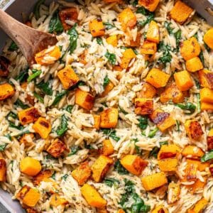 Butternut squash orzo with spinach in a pot with a wooden spoon.