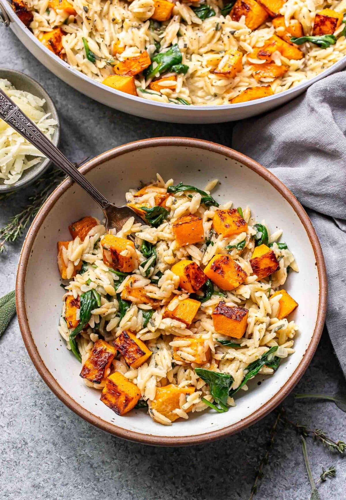 Creamy orzo with butternut squash and spinach in a white bowl with a fork.