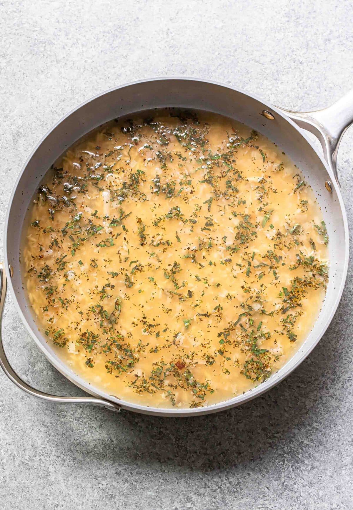 Orzo, shallots, herbs, and broth in a skillet.