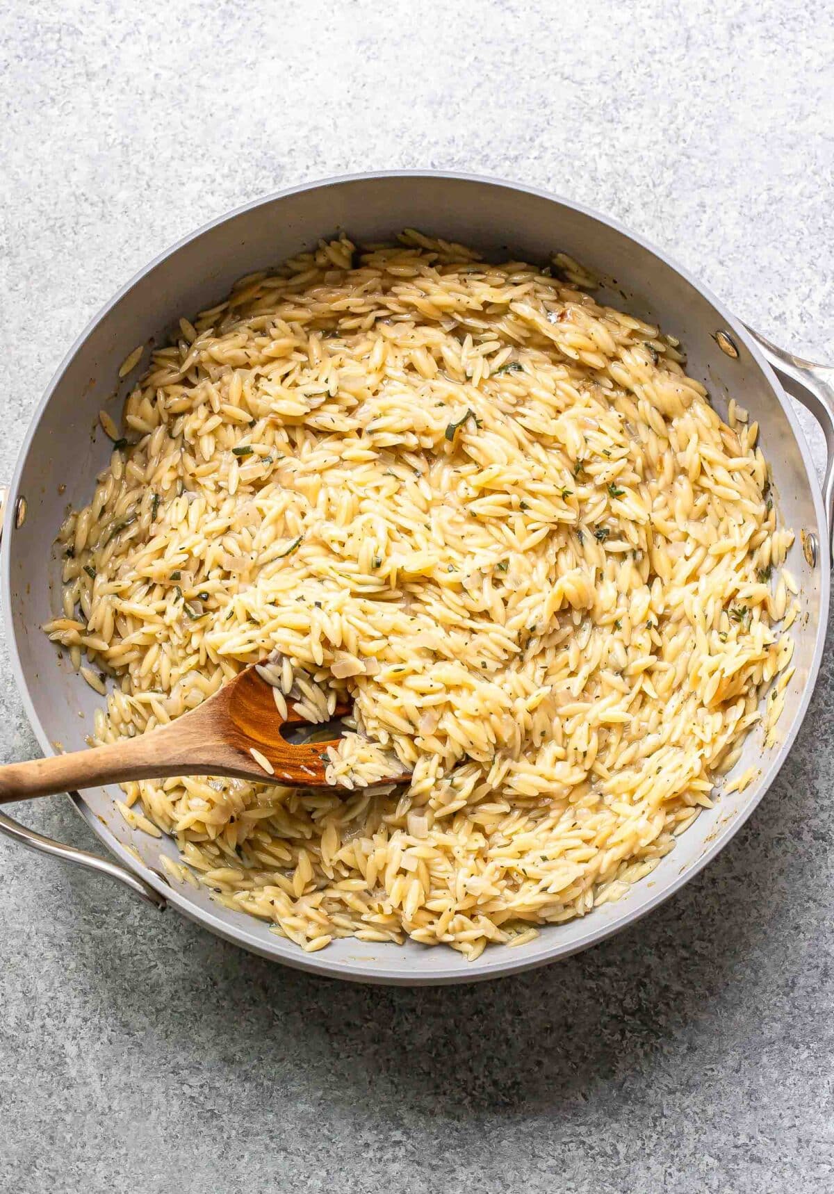 Creamy orzo in a skillet with a wooden spoon.