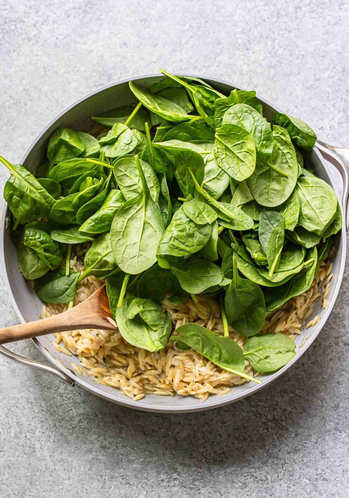 Creamy orzo in a skillet with spinach leaves on top.
