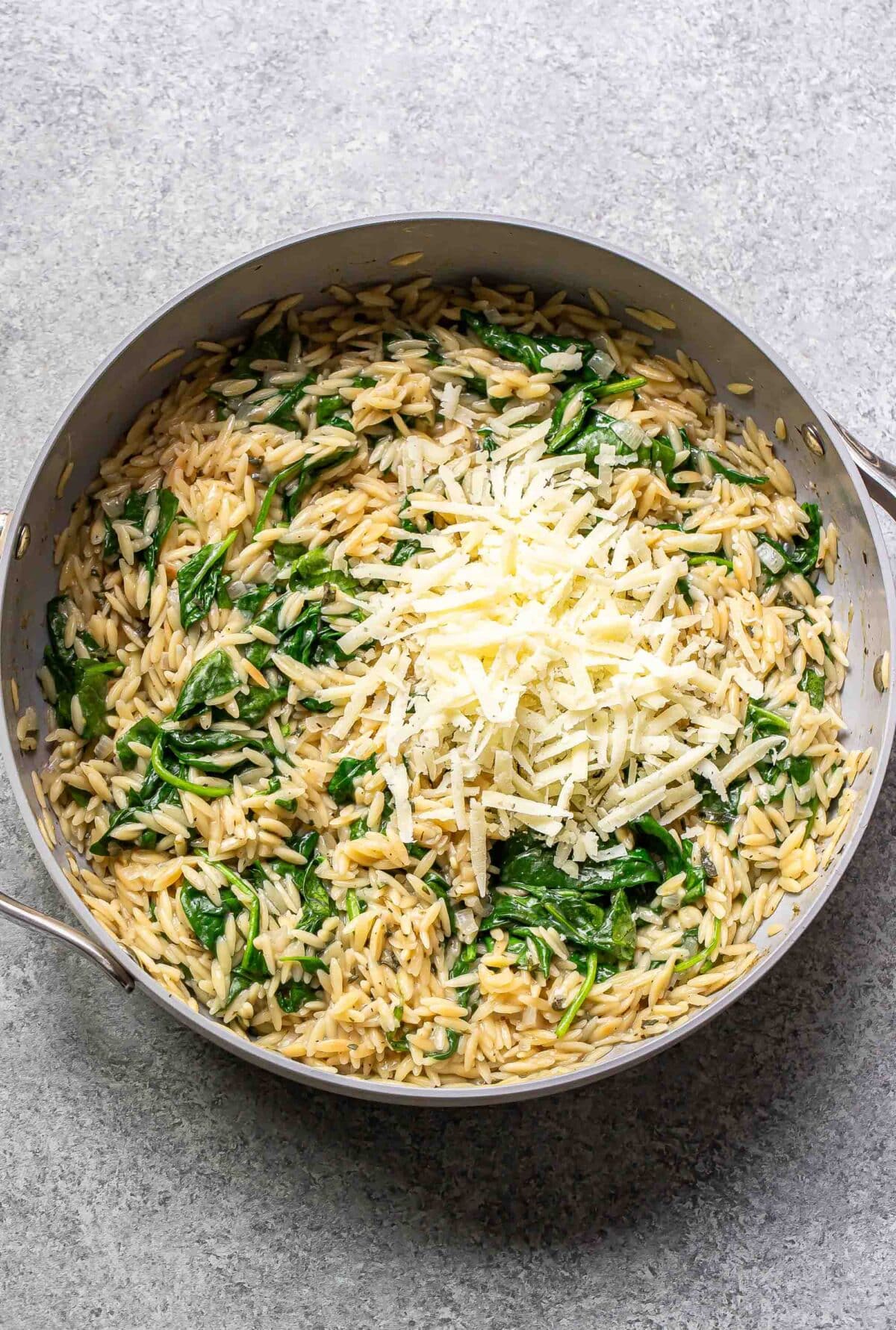Creamy orzo with spinach in a skillet with shredded cheese on top.