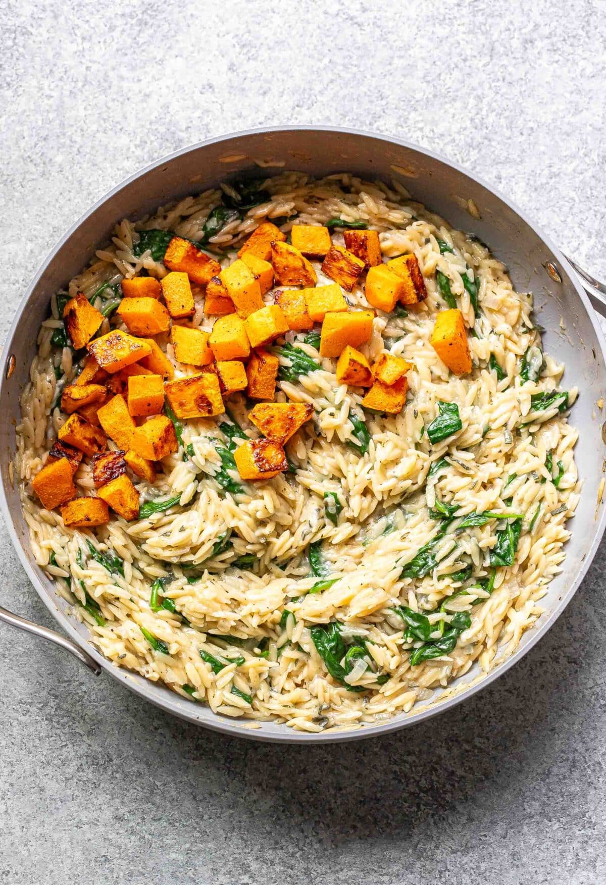 Creamy orzo with spinach in a skillet with roasted butternut squash on top.