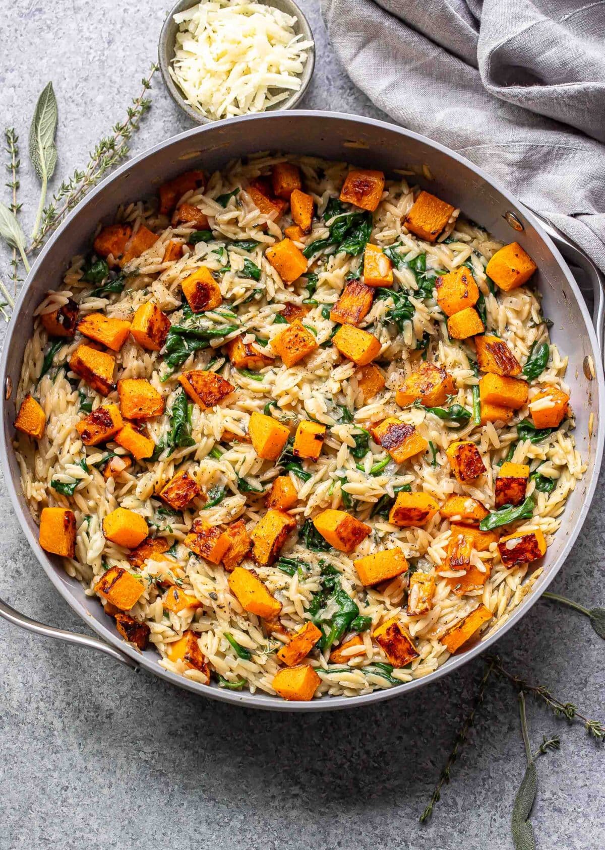 Butternut squash orzo with spinach in a skillet.