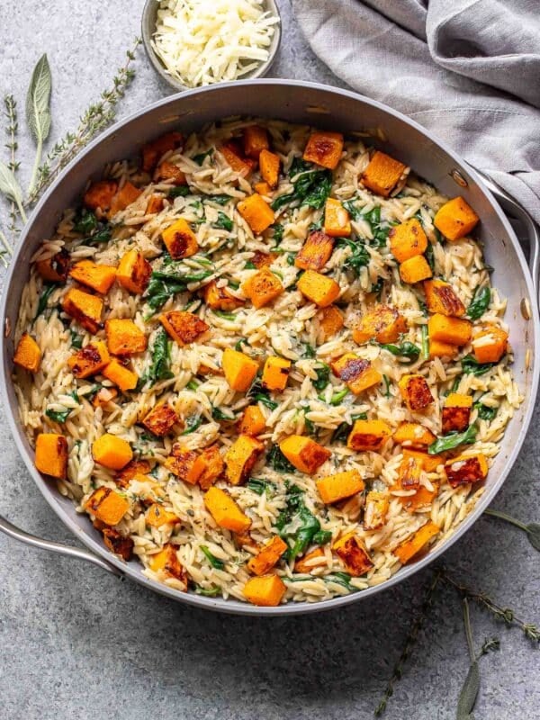 Butternut squash orzo with spinach in a skillet.