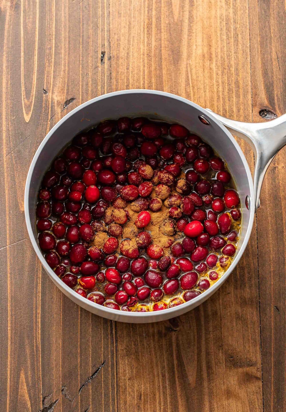 Fresh cranberries, cinnamon, orange juice, and water in a saucepan.