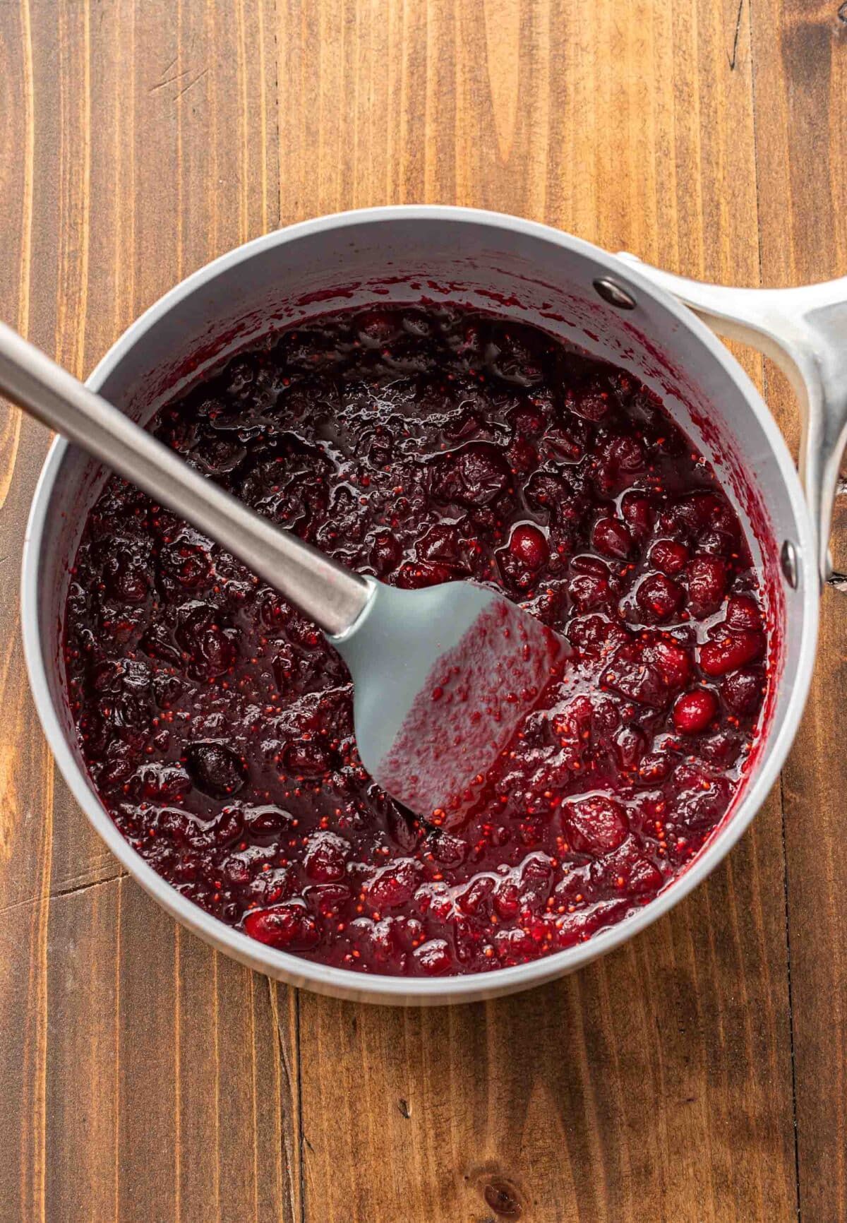 Cranberry sauce in a saucepan with a rubber spatula.