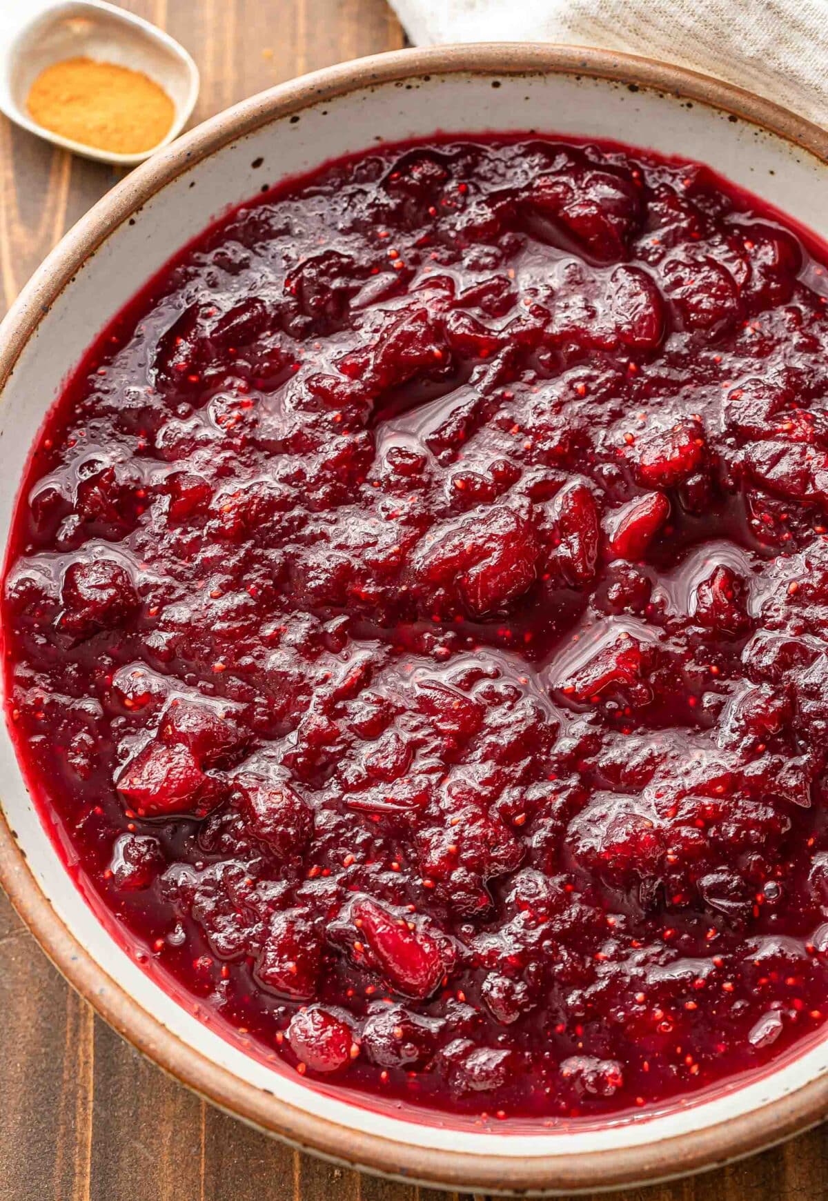 Cranberry sauce in a white bowl with a teaspoon of cinnamon behind it.