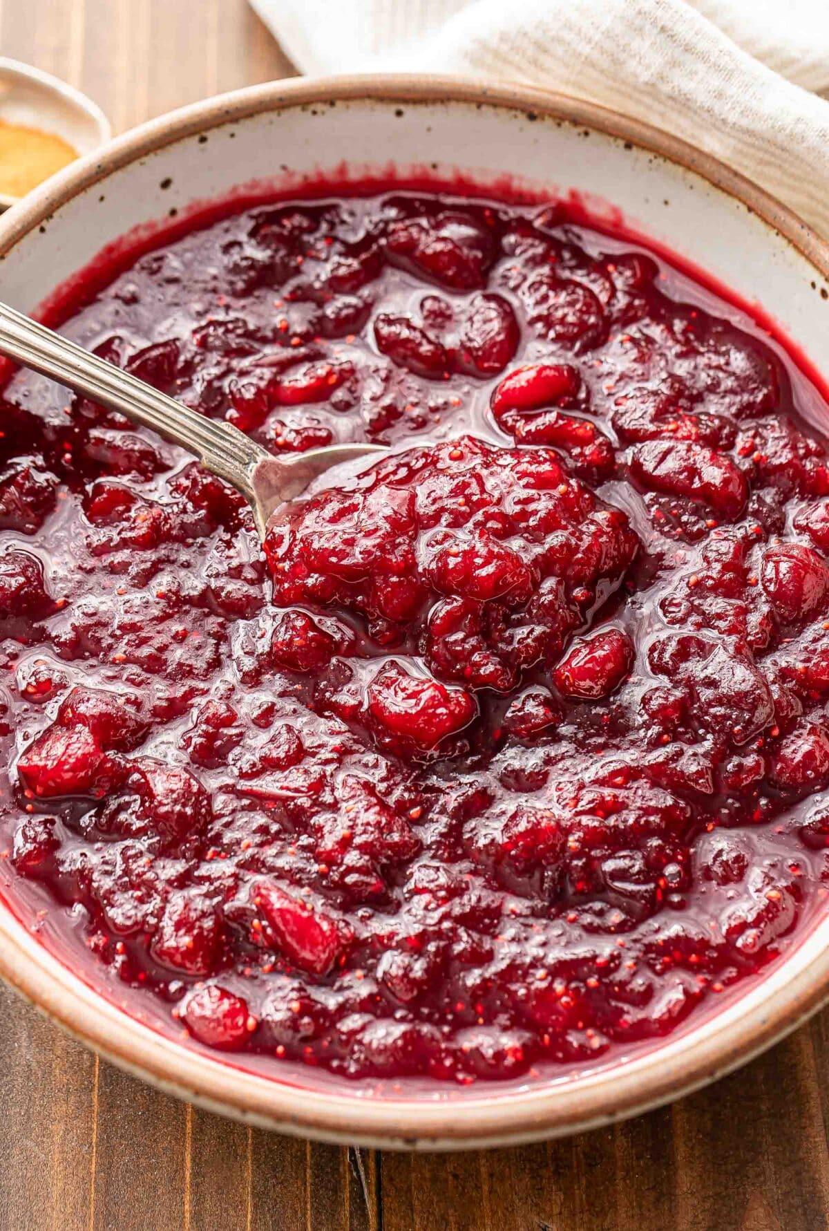 A white bowl with cranberry sauce and a spoon in it.