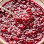 A white bowl with cranberry sauce and a spoon in it.