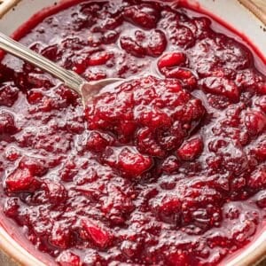A white bowl with cranberry sauce and a spoon in it.